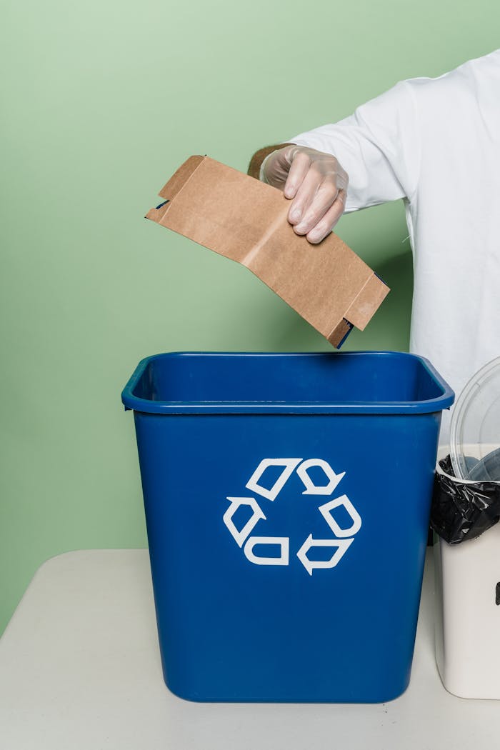 Person placing cardboard into blue recycling bin in indoor setup.